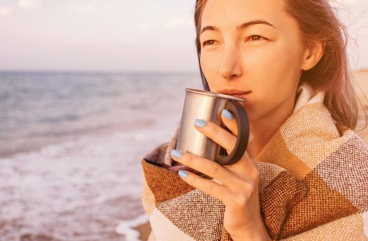 Portrait of young woman with cup of drink on sea coast at sunset.