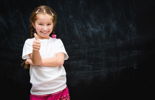 cute happy little girl with thumbs up on the background of the school board