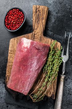 Raw Beef Tenderloin fillet meat on butcher wooden board. Black background. Top view.