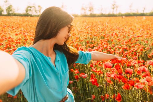 Smiling beautiful young woman taking selfie in poppies meadow on sunny day, point of view.