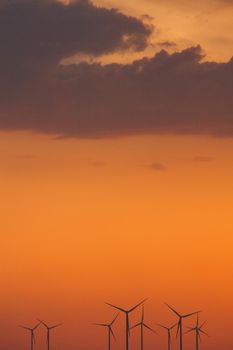 Wind turbine power generators silhouettes at ocean coastline at sunset. Alternative renewable energy production