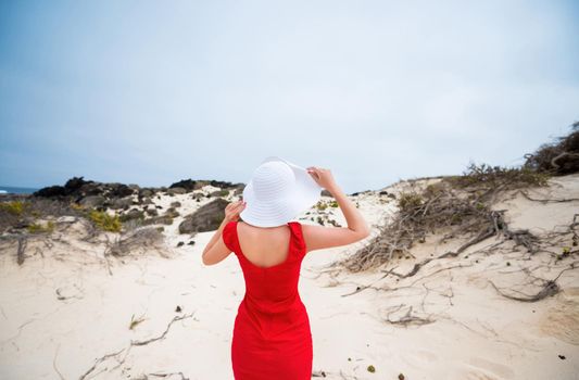 beautiful young woman in evening red dress and white hat on a background of a sand desert