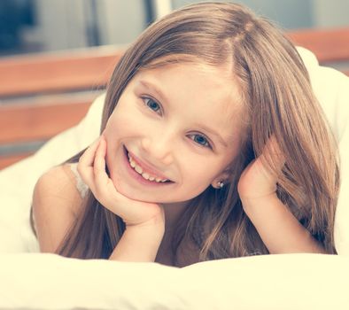 cute little girl lying in a bad under a blanket and smiling