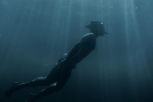 Young man swimming underwater in blue sea among sunbeams, sea vacations.