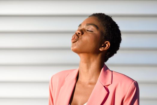 Black woman, with very short hair blowing a kiss. African american female wearing suit with pink jacket with sunset light.