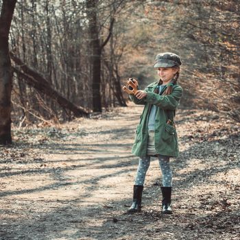 little girl playing with a slingshot in the woods, photo in vintage style