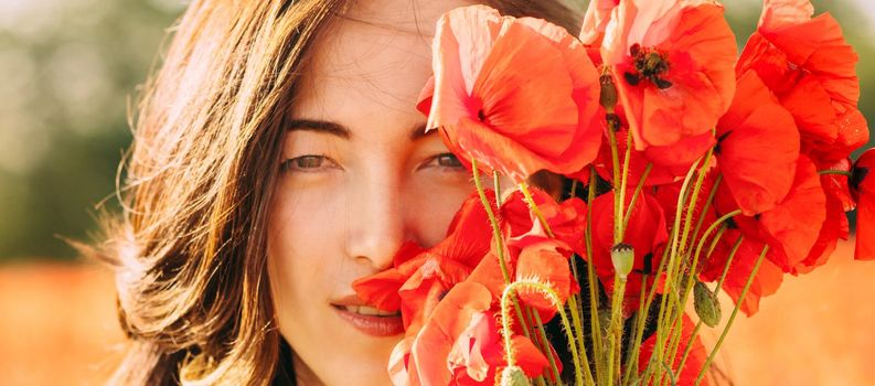 Closeup portrait of beautiful brunette young woman with bouquet of red poppies flower on sunny summer day, looking at camera.