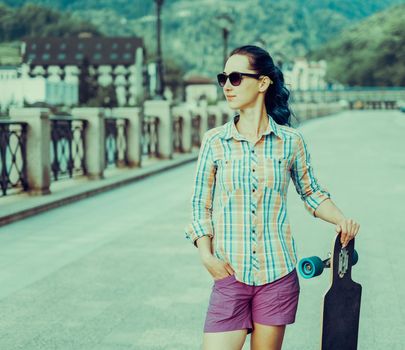 City style girl in sunglasses standing with longboard on street.
