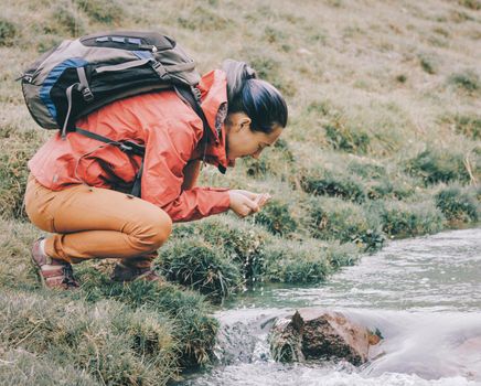 Hiker backpacker young woman drinking water from creek with her hands.