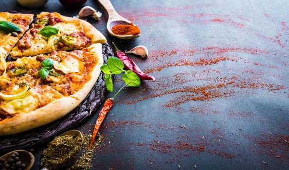 tasty pizza on a black background with spices and vegetables