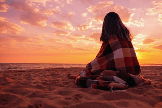 Unrecognizable young woman relaxing on sand beach near the sea at sunset.