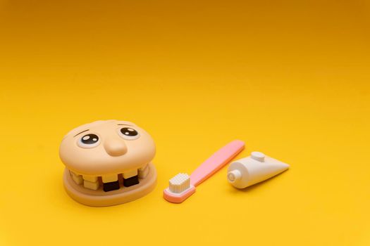 Medical dental children toy, jaw, teeth, toothbrush and toothpaste on yellow background, kids toy concept, copy space.