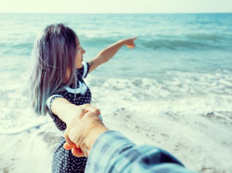 Beautiful young woman holding man's hand and pointing at sea, point of view. Focus on male hand.