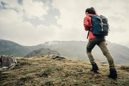 Explorer young woman with backpack going up on mountain outdoor.