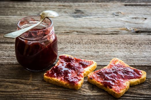 bread with jam and a jar of jam on wooden background, breakfast