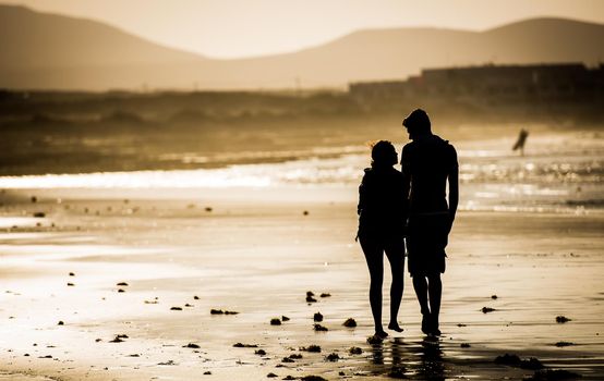 Silhouette of the loving couple, walking on the beach