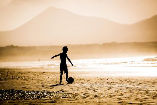 Silhouette of boy on the beach, playing football