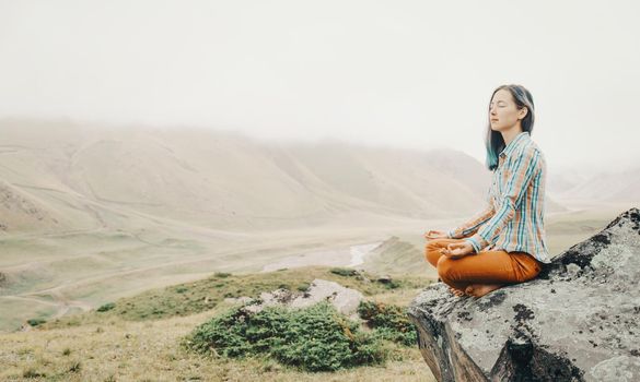 Young woman relaxing on edge of cliff in pose of lotus in the mountains.