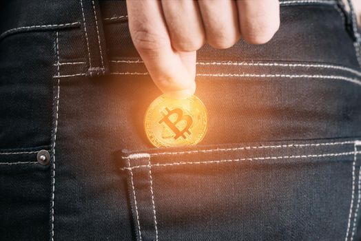 Hand putting gold bitcoin into pocket of jeans, symbol of crypto currency, close-up.