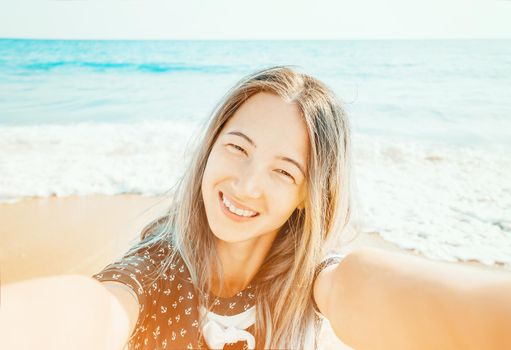 Smiling girl taking selfie on background of sea on summer beach vacations, point of view.