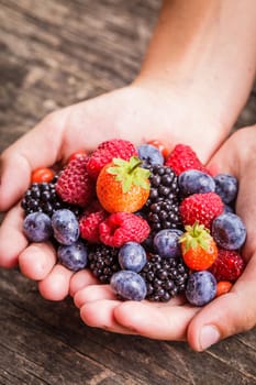 Summer wild berries in hands - raspberry, strawberry, blackberry and blueberry