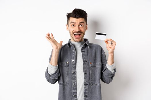 Excited man scream from joy and showing plastic credit card, rejoicing on shopping, standing against white background.