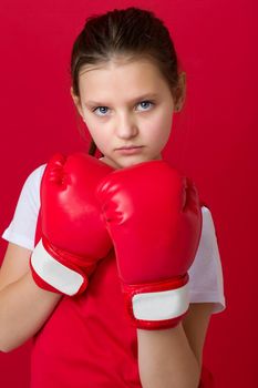 Teenage girl posing in boxing gloves. Portrait of sportive boxer girl dressed sportswear ready to fight. Child training on red background. Healthy lifestyle, sport and fitness concept