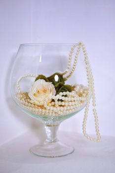 White pearls and white roses in the glass String of white pearls in a glass on the table