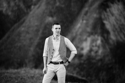 a young guy in a brown suit on the background of mountain green slopes near the old riverbed