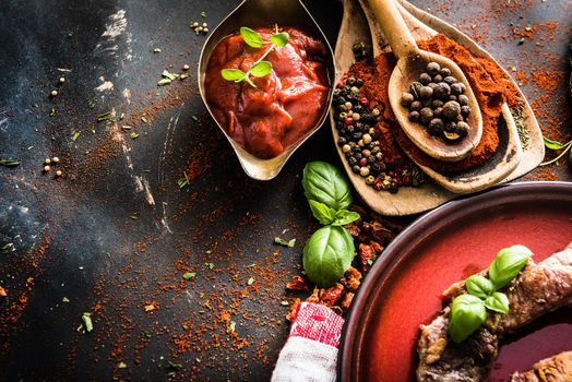 grilled meat on a plate with tomato sauce, spices on textured black background