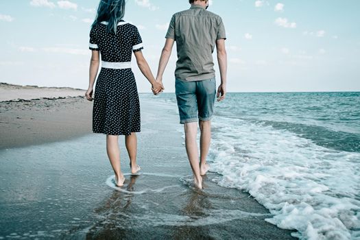 Young loving couple walking on sand coast near the sea and holding hands together, beach summer vacations.