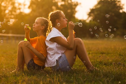 Two teenage girls have fun in the park. Two friends outdoor. Summer people doing bubbles