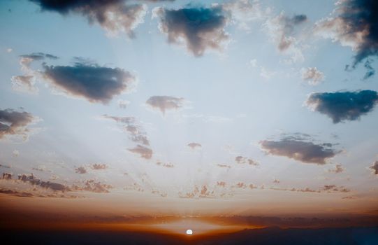 Beautiful sky with cumulus clouds at sunset, sun over horizon.