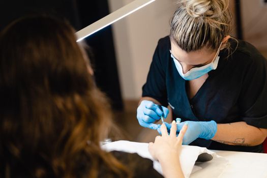 Close-up of Beautician painting her client's nails in blue and yellow nail varnish in a beauty centre