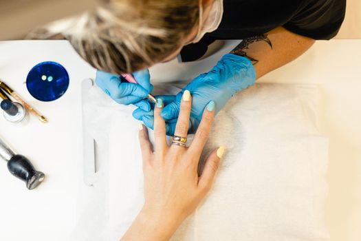 Close-up of Beautician painting her client's nails in blue and yellow nail varnish in a beauty centre