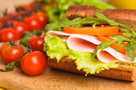 Wholegrain sandwich with ham, tomato, lattuce and arugula with glass of orange juice. Breakfast