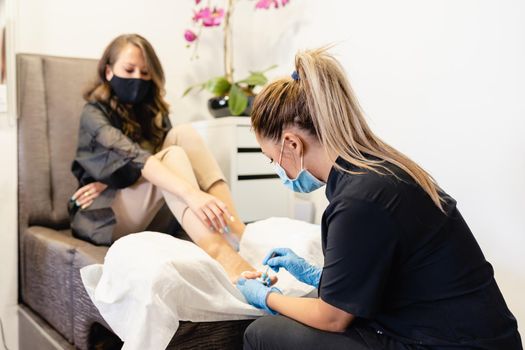 Beautician giving a pedicure painting her client's nails in a beauty centre. Business and beauty concepts