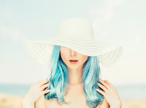 Attractive stylish young woman with blue hair in a hat with wide brim on background of sea coastline.