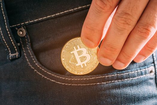 Hand putting bitcoin into pocket, symbol of crypto currency and virtual money, close-up.