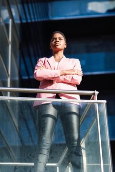 Black businesswoman standing near business office building. African american female wearing suit with pink jacket.