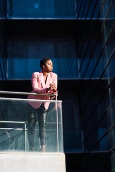 Black businesswoman standing near business office building. African american female wearing suit with pink jacket.