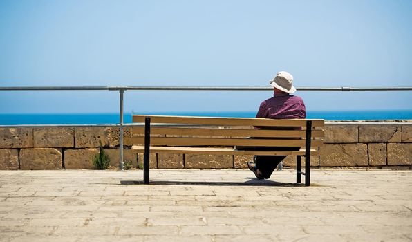 man sitting on a bench of an embarkment watching the ocean