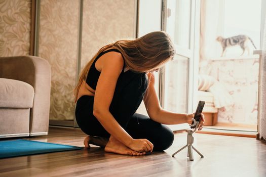 Young woman with long hair, fitness instructor in black sportswear, doing stretching and pilates on yoga mat at home. Female fitness yoga routine concept. Healthy lifestyle harmony and meditation