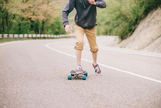 Unrecognizable guy riding on longboard on winding asphalt road outdoor.