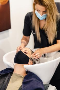 Female hairdresser washing a client's head in a salon, protected by a mask against Covid-19