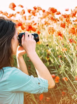 Photographer young woman taking photographs with camera in poppies meadow, side view.