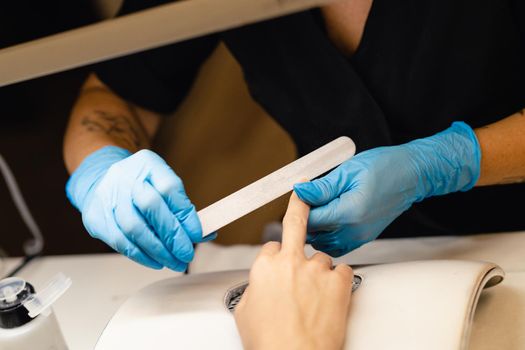 Aesthetician doing the manicure, filing the nails with a file to his client in a beauty center. Business and beauty concepts