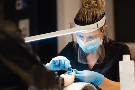 Aesthetician doing the manicure, filing the nails with a file to his client in a beauty center. Business and beauty concepts