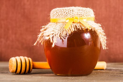 Honey in jar with wooden dripper on the table