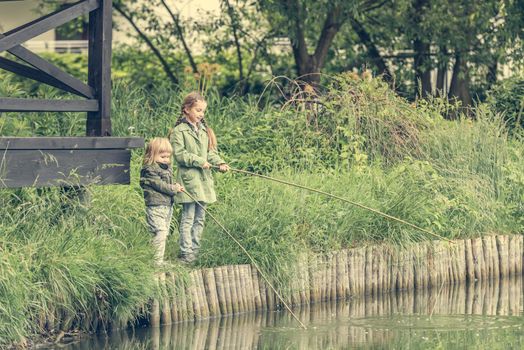 two little fisher girls with rods on a river bank